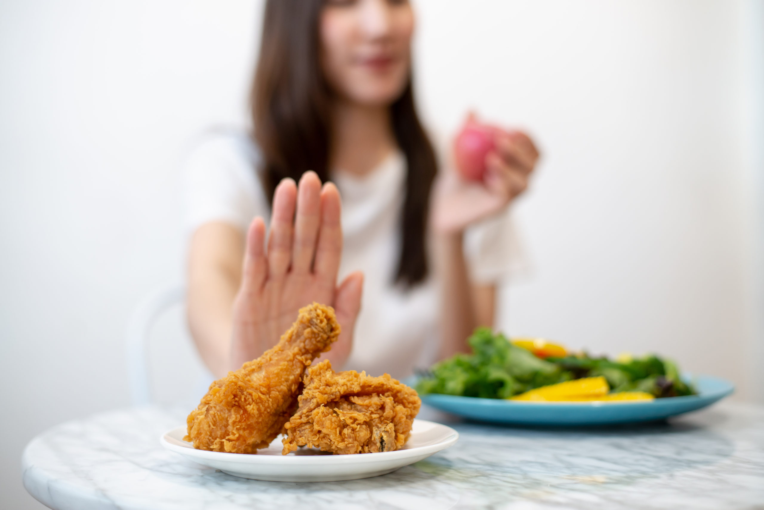 Donna a tavola che sceglie alimenti sani e respinge un piatto di pollo fritto, per combattere l'enterite